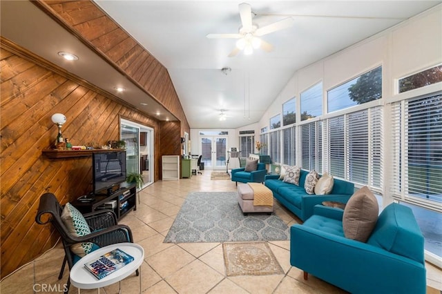 tiled living room featuring lofted ceiling, a ceiling fan, wood walls, and french doors