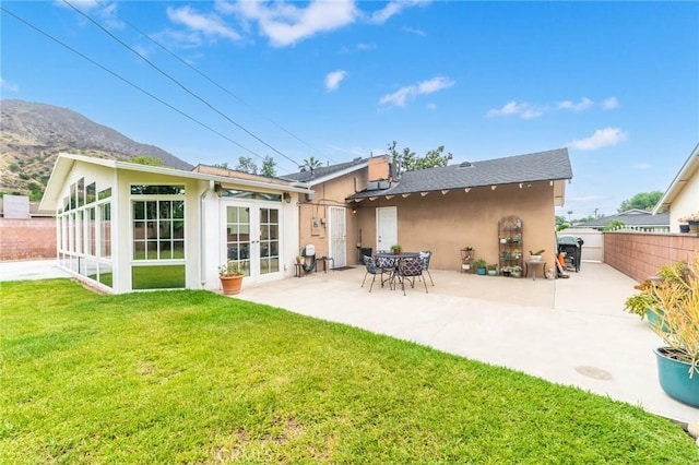 back of property with stucco siding, a lawn, a patio, fence, and french doors