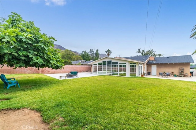 rear view of property featuring a yard, a sunroom, stucco siding, and a patio area