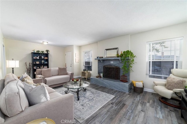 living area with a fireplace with raised hearth, a textured ceiling, baseboards, and wood finished floors