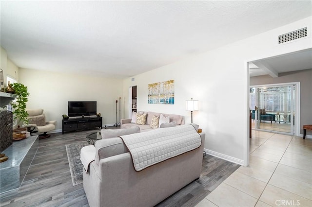 living room with beamed ceiling, light wood-style flooring, baseboards, and visible vents