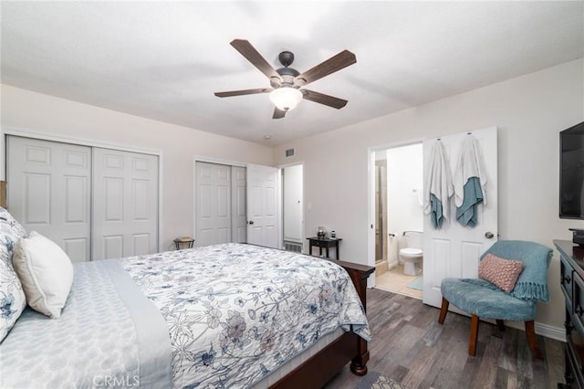 bedroom featuring visible vents, multiple closets, ensuite bathroom, dark wood finished floors, and baseboards