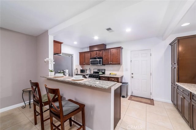 kitchen featuring light stone counters, visible vents, a breakfast bar, a peninsula, and appliances with stainless steel finishes