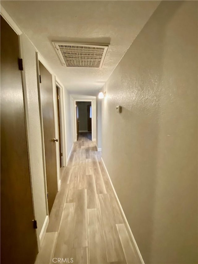 hall featuring light wood-style floors, visible vents, a textured wall, and baseboards