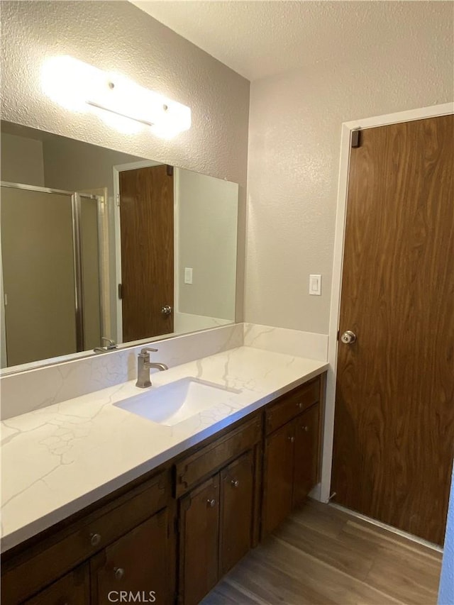 bathroom featuring a stall shower, a textured ceiling, wood finished floors, vanity, and a textured wall