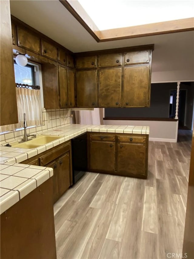kitchen with tile countertops, dishwasher, light wood-type flooring, and a sink