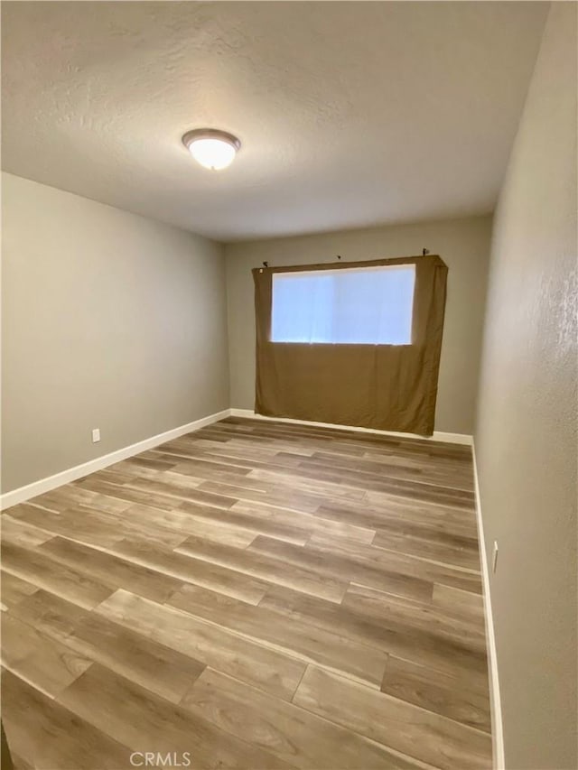 spare room with a textured ceiling, light wood-type flooring, and baseboards