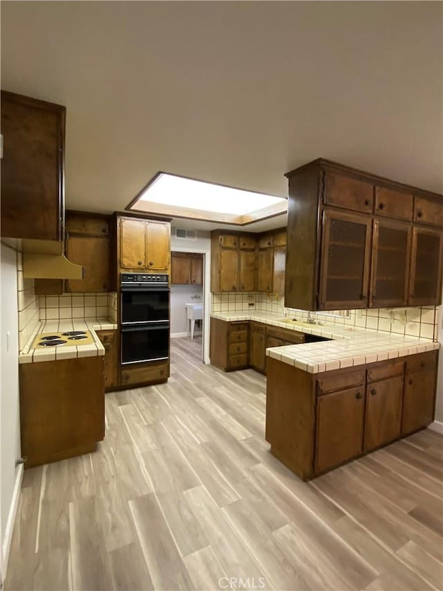 kitchen featuring tile countertops, decorative backsplash, light wood-type flooring, and a peninsula