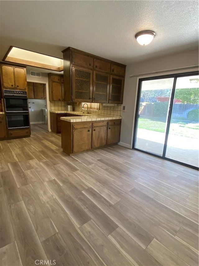 kitchen featuring visible vents, backsplash, light wood-style flooring, a peninsula, and dobule oven black