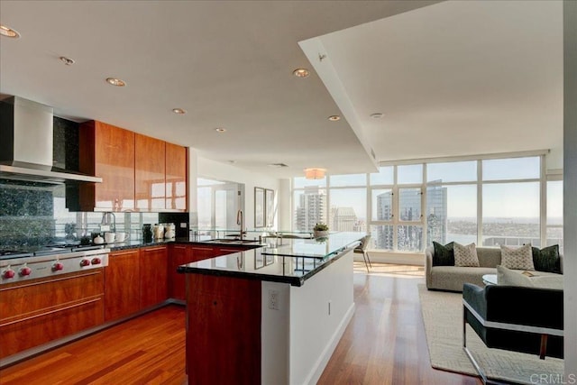 kitchen featuring dark countertops, wall chimney range hood, stainless steel gas cooktop, open floor plan, and a sink
