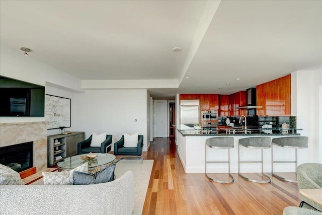 kitchen with light wood finished floors, wall chimney range hood, stainless steel built in refrigerator, open floor plan, and a peninsula