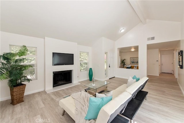 living area with visible vents, beam ceiling, baseboards, a fireplace with raised hearth, and light wood-style flooring