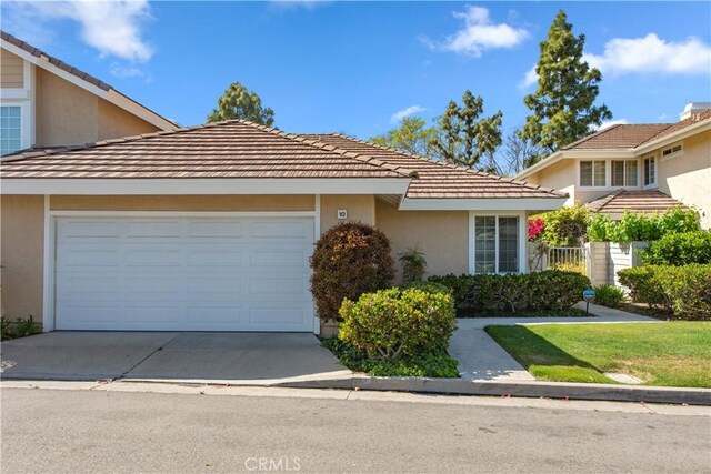 ranch-style house with stucco siding, an attached garage, driveway, and a tile roof