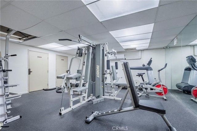 workout area with a wall mounted air conditioner, a paneled ceiling, and baseboards