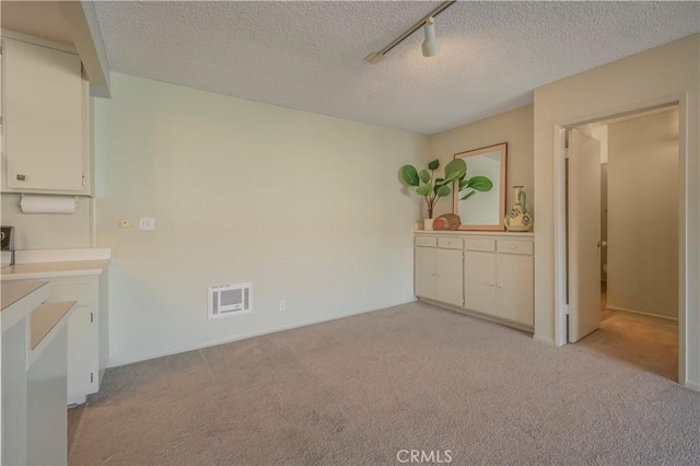 interior space featuring white cabinetry, a textured ceiling, visible vents, and light carpet