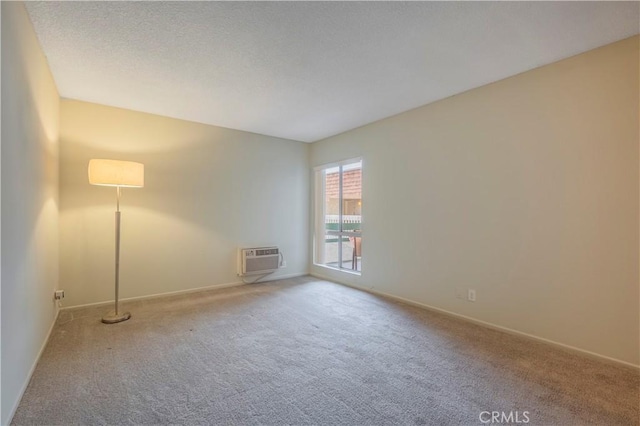 spare room with a textured ceiling, an AC wall unit, baseboards, and carpet floors