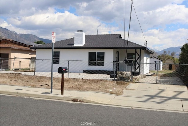 ranch-style home with a gate, a shingled roof, stucco siding, a fenced front yard, and a mountain view