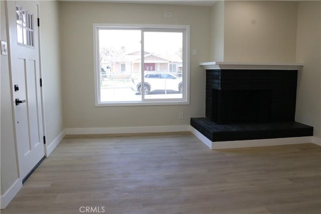 unfurnished living room with baseboards, a fireplace with raised hearth, and wood finished floors