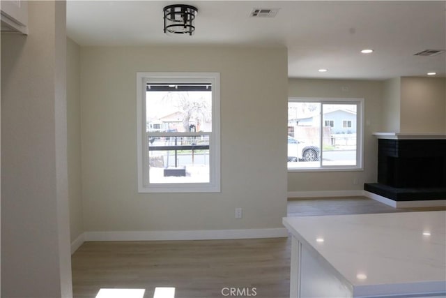 kitchen featuring light wood-type flooring, visible vents, baseboards, and a fireplace with raised hearth