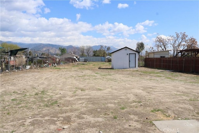 view of yard featuring an outbuilding, a mountain view, a storage shed, and fence