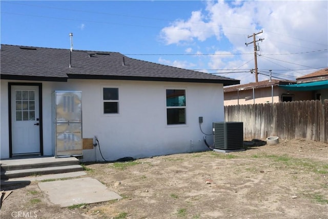 rear view of property featuring roof with shingles, fence, central AC, and stucco siding