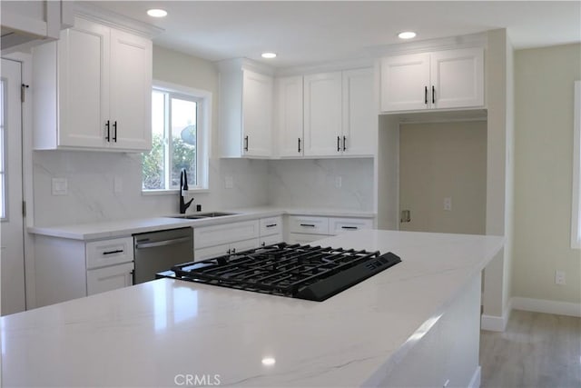 kitchen featuring tasteful backsplash, light stone countertops, dishwasher, white cabinetry, and a sink