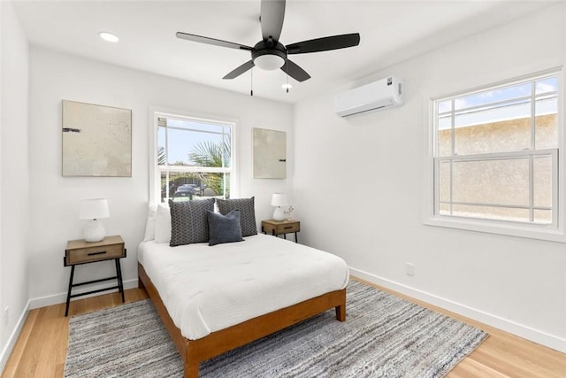 bedroom with baseboards, light wood-type flooring, and a wall mounted AC