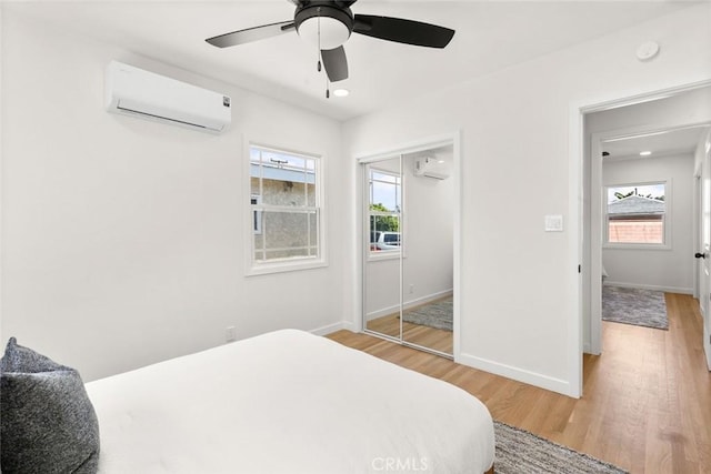 bedroom featuring light wood-style flooring, a wall mounted air conditioner, and multiple windows