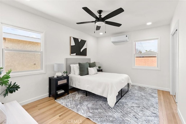 bedroom with multiple windows, light wood finished floors, and a wall mounted air conditioner