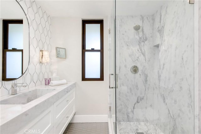 full bath featuring a marble finish shower, baseboards, vanity, and tile patterned flooring