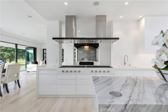 kitchen featuring gas cooktop, a sink, white cabinetry, wall chimney range hood, and modern cabinets