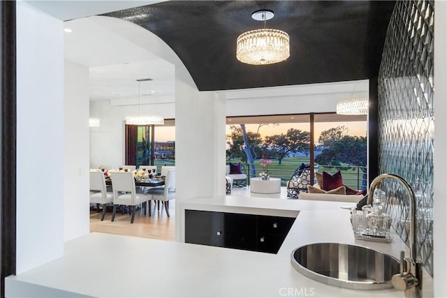 kitchen featuring a chandelier, pendant lighting, wood finished floors, arched walkways, and a sink