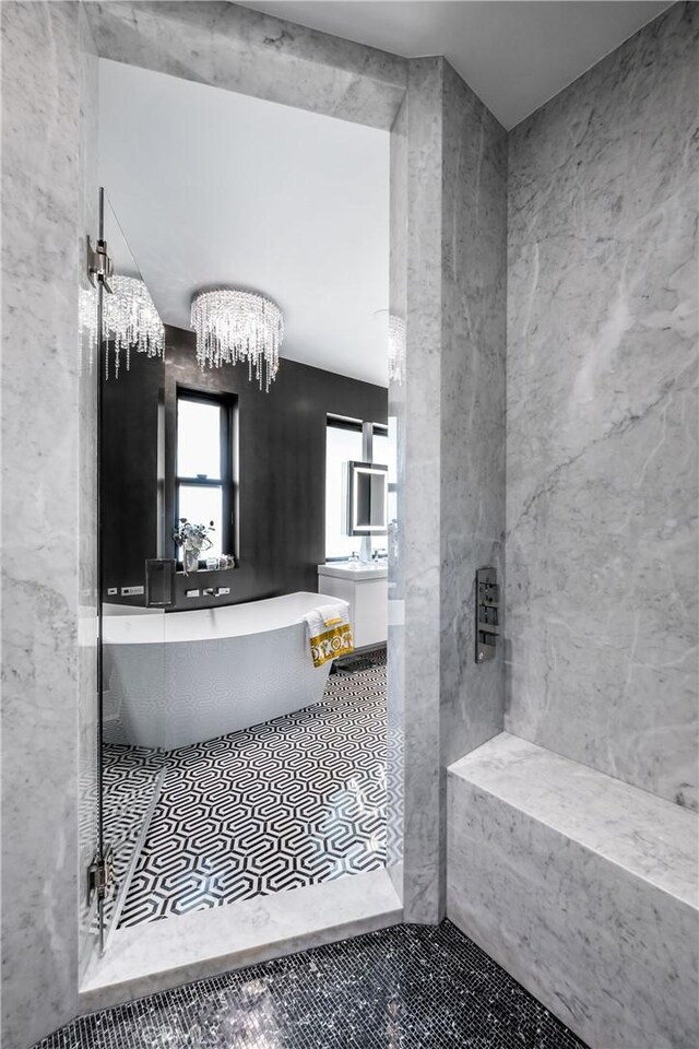 bathroom with a notable chandelier, a freestanding bath, and tile patterned flooring