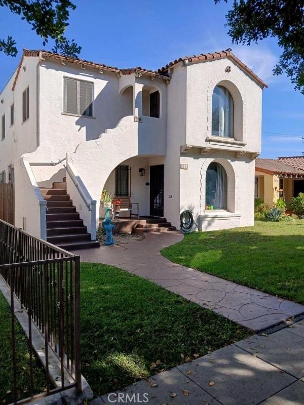 rear view of house featuring stucco siding, a tile roof, fence, stairway, and a yard