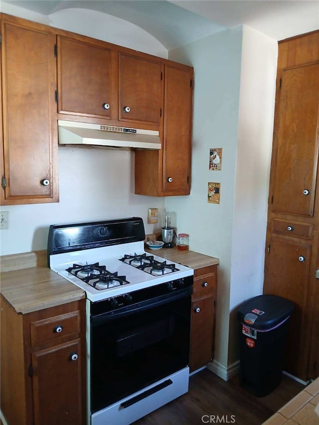 kitchen with under cabinet range hood, range with gas stovetop, brown cabinetry, and light countertops