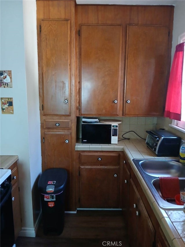 kitchen with tile counters, brown cabinets, stove, and a sink