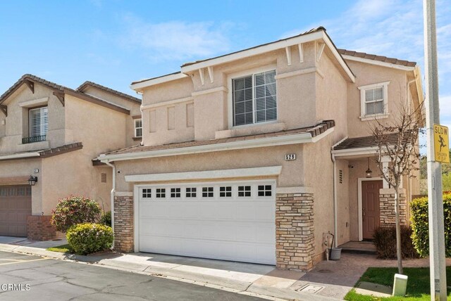 view of front facade featuring a tiled roof, a garage, stone siding, and stucco siding