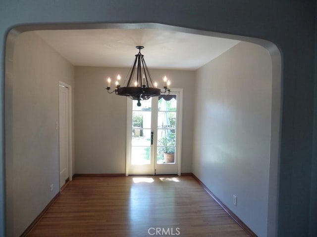 unfurnished dining area with arched walkways, a notable chandelier, baseboards, and wood finished floors