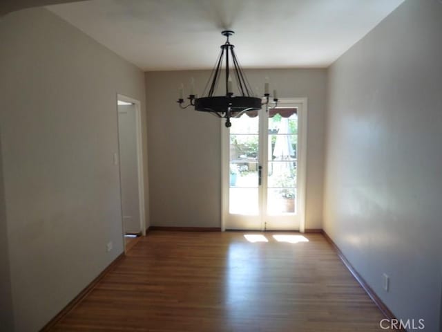 unfurnished dining area with a notable chandelier, wood finished floors, baseboards, and french doors