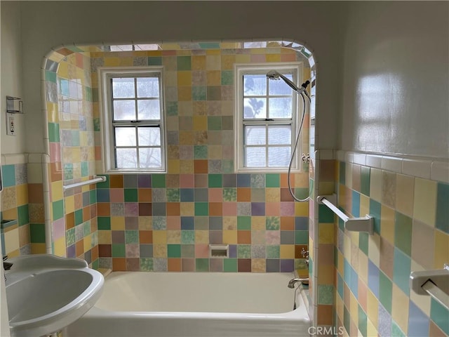 bathroom with a wainscoted wall, tub / shower combination, tile walls, and a sink