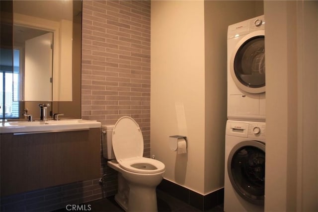 half bath featuring vanity, tile walls, toilet, and stacked washer and clothes dryer