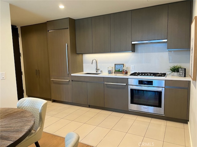 kitchen with under cabinet range hood, appliances with stainless steel finishes, light countertops, and a sink