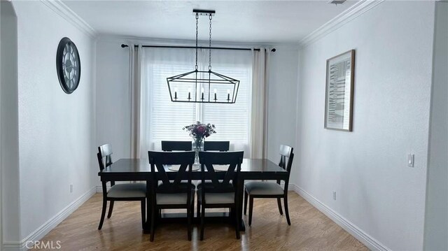 dining room with a chandelier, light wood-type flooring, crown molding, and baseboards