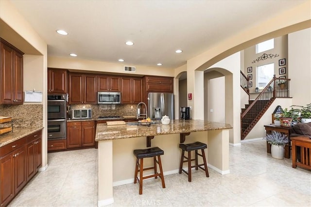 kitchen featuring visible vents, decorative backsplash, arched walkways, stainless steel appliances, and a sink