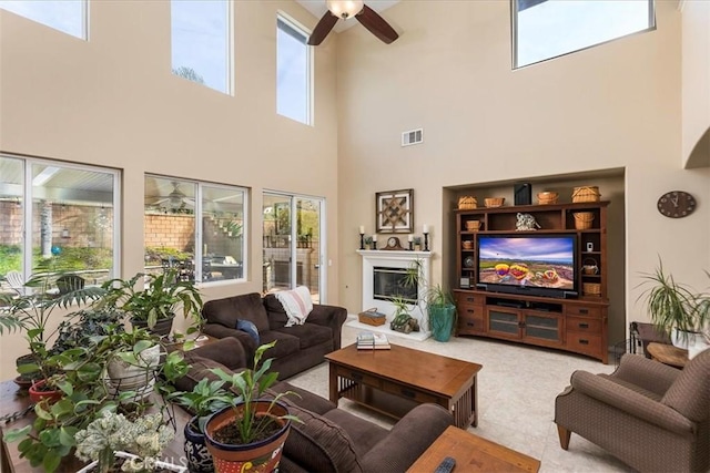 living room with a glass covered fireplace, visible vents, and ceiling fan