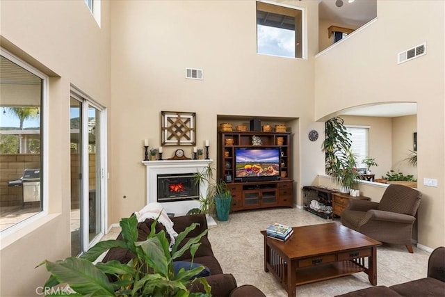 living room with visible vents, arched walkways, a lit fireplace, and a towering ceiling