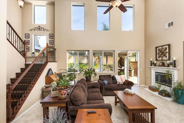 tiled living area with baseboards, visible vents, ceiling fan, stairs, and a glass covered fireplace