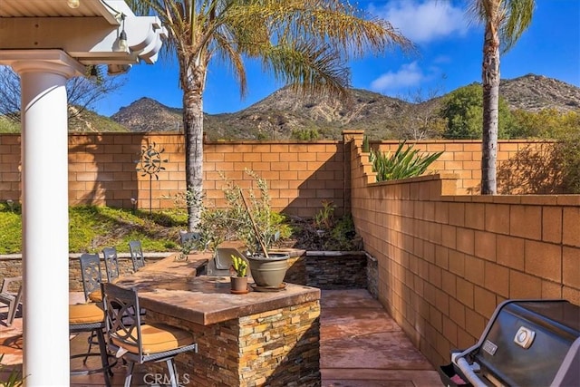 view of patio / terrace featuring outdoor dry bar, a grill, a mountain view, and a fenced backyard