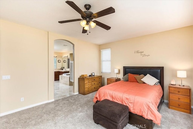 bedroom featuring connected bathroom, baseboards, ceiling fan, light colored carpet, and arched walkways