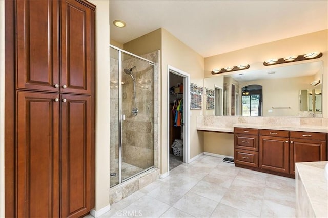 bathroom featuring baseboards, vanity, a spacious closet, and a shower stall